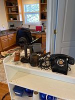 Wide view of the lot on a white shelf with background of kitchen, showing all items together: two telephones, locomotive oiler, and collectible knife.