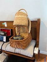 Woven baskets stacked with metal button tin inside rectangular basket on cushioned bench.