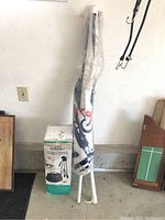 Photo of wrapped Coors Light beach umbrella with metal pointed legs beside the box of Merkury Innovations video camera essentials kit tripod.