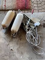 Photo showing two boat dock bumpers, boat anchor with rope, and mini hand puller with red handle on concrete floor.