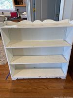 Front view of a white painted wood bookcase displaying three shelves and paint chips throughout.