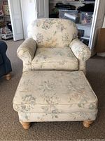 Front view of floral upholstered armchair with matching ottoman in front, showing fabric pattern and wooden legs.