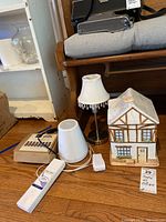 Photo showing essential oil diffuser, boxes of essential oils, small fabric-shaded lamp with hanging crystals, and ceramic house cookie jar on wooden floor.