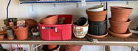 Shelf with multiple flower pots, plastic container, and gardening supplies inside