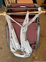 Cloth pod hammock hanging over two folded maroon fabric Summer Winds gravity chairs.