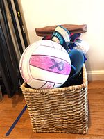 Wicker basket containing a white volleyball with pink stitching, rollerblades, hat, and other items.