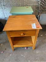 Natural wood side table with drawer and open shelf showing surface wear and chipped finish.