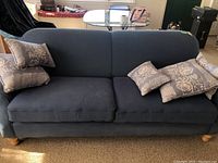 Front view of the blue 2-cushion sofa with five blue and white patterned throw pillows placed on it.