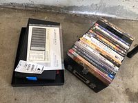 Black Moderno MS4/MS6 speaker selector box with instruction manual on top, alongside a stack of DVDs in plastic cases with titles visible.