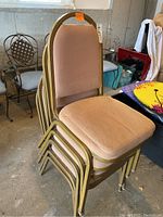 Photo of five light brown padded stacking chairs with gold-colored metal frames, showing wear and dirt, stacked together.