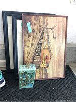Three framed train-themed wall art pieces stacked with a small vintage Avon bottle in front.