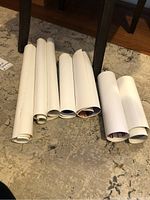 Seven rolled posters or photos on carpet floor arranged in a row.