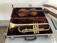 Photo showing vintage brass trumpet and wooden violin inside a fitted brown velvet-lined case.