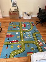 Full view of the child's area rug showing the layout of roads, traffic signs, and buildings on blue background against hardwood floor