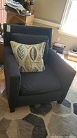Navy blue upholstered armchair with a decorative leaf-patterned throw pillow on the seat facing forward.