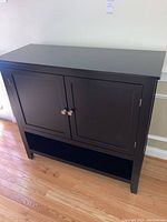 Front view showing the black buffet cabinet with two doors and lower shelf on wooden floor.