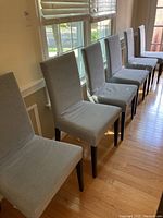 Six light gray upholstered chairs with straight backs and dark wooden legs arranged in a row