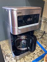 Front and angled view of the Braun 12-cup coffee maker showcasing stainless steel finish, glass carafe, and digital control panel.