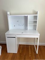 Front view of white child's desk with hutch and whiteboard. Desk has two shelves on right side of hutch, one drawer, and closed cabinet on left side.