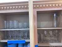 Two sets of shelves with various clear glassware: top left shelf has multiple tall glasses, bottom left shelf has shorter glasses; right shelves have one glass pitcher at the top with six large wine glasses beneath.