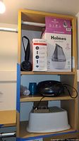 Full shelf view showing boxed Holmes humidifier, Revlon blow dryer box and unit, black Sylvania CD player and white children's stool beneath
