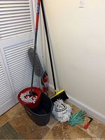 Full view of the mop, bucket, broom, gloves, and mop heads arranged against wall.