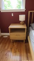 Front view of oak nightstand with a small lamp on top, showing drawer and open shelf