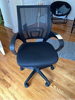Front view of a black mesh office chair with padded seat and armrests on wood flooring.