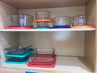 Glass mixing bowls and bakeware dishes with assorted colored plastic lids arranged on shelves.