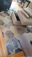 Photo of grey and black geometric area rug partially under furniture showing pattern and condition