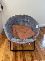 Gray saucer chair with plush padded seat and two brown cushions placed on it, sitting on hardwood floor.