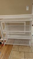 Front view of white wire mesh shelving unit showing overall structure and three mesh shelves.