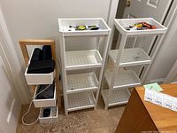 Two white plastic shelving units and one wooden storage rack shown together in room corner on floor with tiled floor and white wall