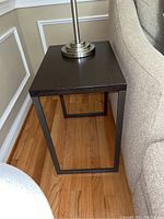 Side view of metal side table showing rectangular black wood top and black metal frame base.