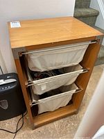 Front view of wood storage cabinet with three cloth bags inside, showing overall condition and wood surface
