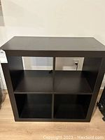 Front view of black cubby storage shelf highlighting four empty square compartments.