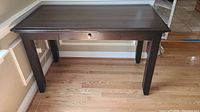 Full view of the dark wooden desk table showing the top, legs and central drawer with chip on the side noted.