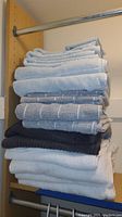 Stack of assorted bath towels, hand towels, and washcloths folded on shelf showing colors and textures