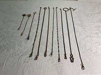 Photo showing eleven vintage pocket watch chains arranged flat on fabric background, displaying varied length and clasp styles.