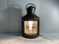 Front view of antique brass ship light showing prism lens lit up and handle on top.