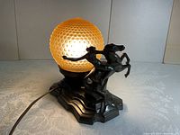 Front angled view of black metal lamp with woman on horse sculpture and amber honeycomb-patterned glass globe lit up