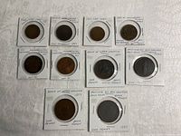 Coins and tokens laid out on white surface, each in protective holders with handwritten labeling including dates and origins such as Bank of Upper Canada and Danish coins.