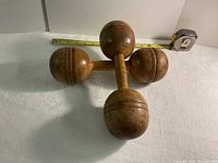 Pair of antique wooden bar bells laid crosswise on a white surface with a measuring tape showing approximately 11 inches long each.