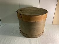 Full front view of the antique wooden cheese box showing its round shape and wooden band.