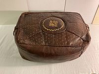 Top view showing the embroidered circular patch with geometric stitching and small dots pattern on the dark brown leather pouffe.