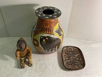 Photo showing Talking Earth vase in center, Inuit pottery person on left and Haida bear dish on right.