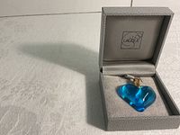 Pendant displayed in open grey Lalique box showing pendant and packaging.