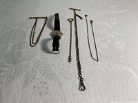 Full view of Olar wristwatch with attached leather band and four metal pocket watch chains in various styles and lengths.