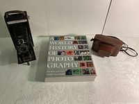 Photo showing the No. A1 Autographic Kodak Jr. folding camera, the photography history book, and Kodak Pony 135 camera in leather case