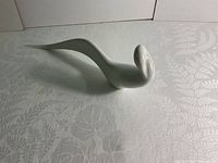 Front angle view of the white porcelain bird figurine on a patterned surface showing its smooth shape and long tail.